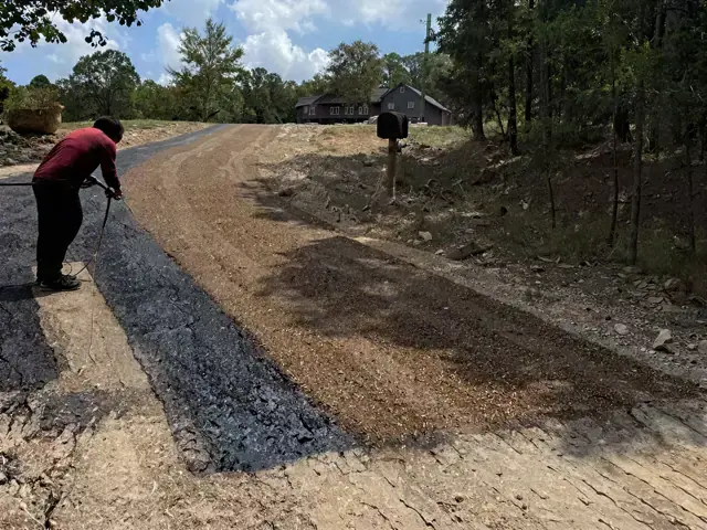 Worker pulling a hose along a fresh gravel driveway in the woods