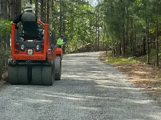 Ride-on roller compacting a gravel road through the woods