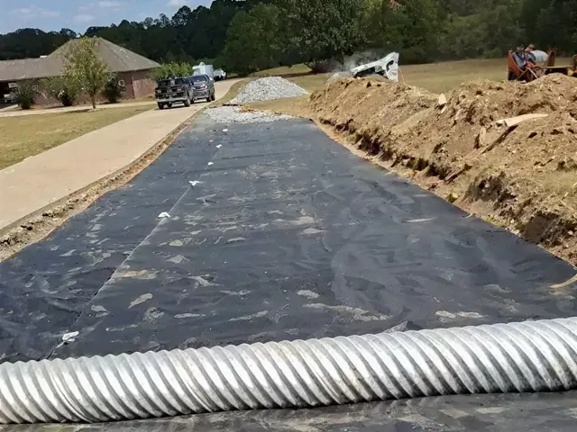 Asphalt being laid over a prepared base between graded shoulders